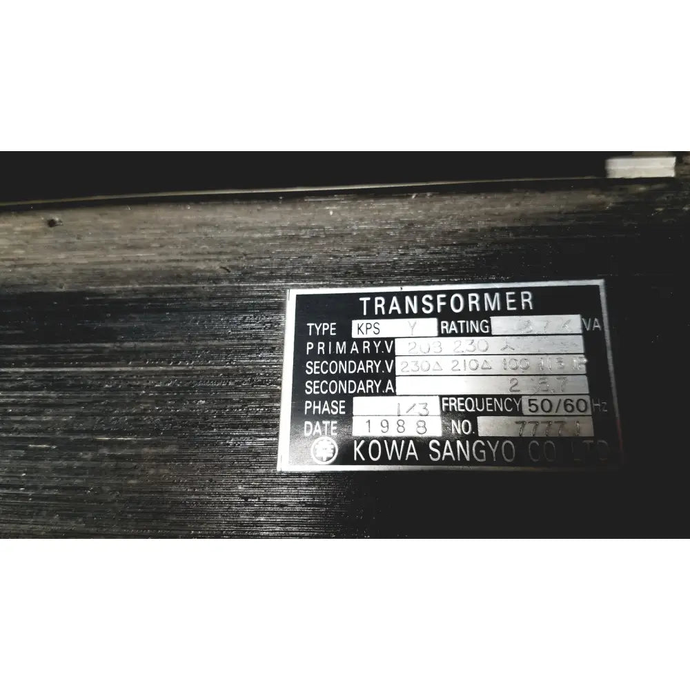 Silver metallic label on a dark surface showing technical specifications for kowa sangyo power transformers reuse medical product