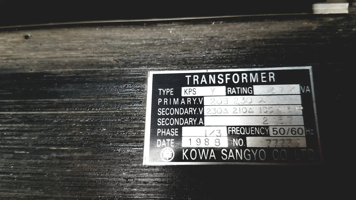 Silver metallic label on a dark surface showing technical specifications for kowa sangyo power transformers reuse medical product