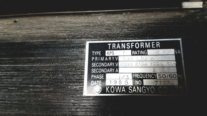 Silver metallic label on a dark surface showing technical specifications for kowa sangyo power transformers reuse medical product