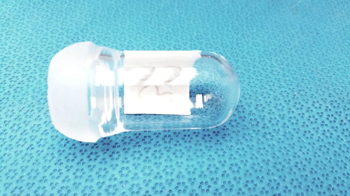 Clear glass lab spherical joint stopper with frosted white cap and small white label affixed to the side