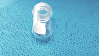Clear plastic baby bottle with white label and threaded screw cap shown alongside lab spherical joint glass stoppers
