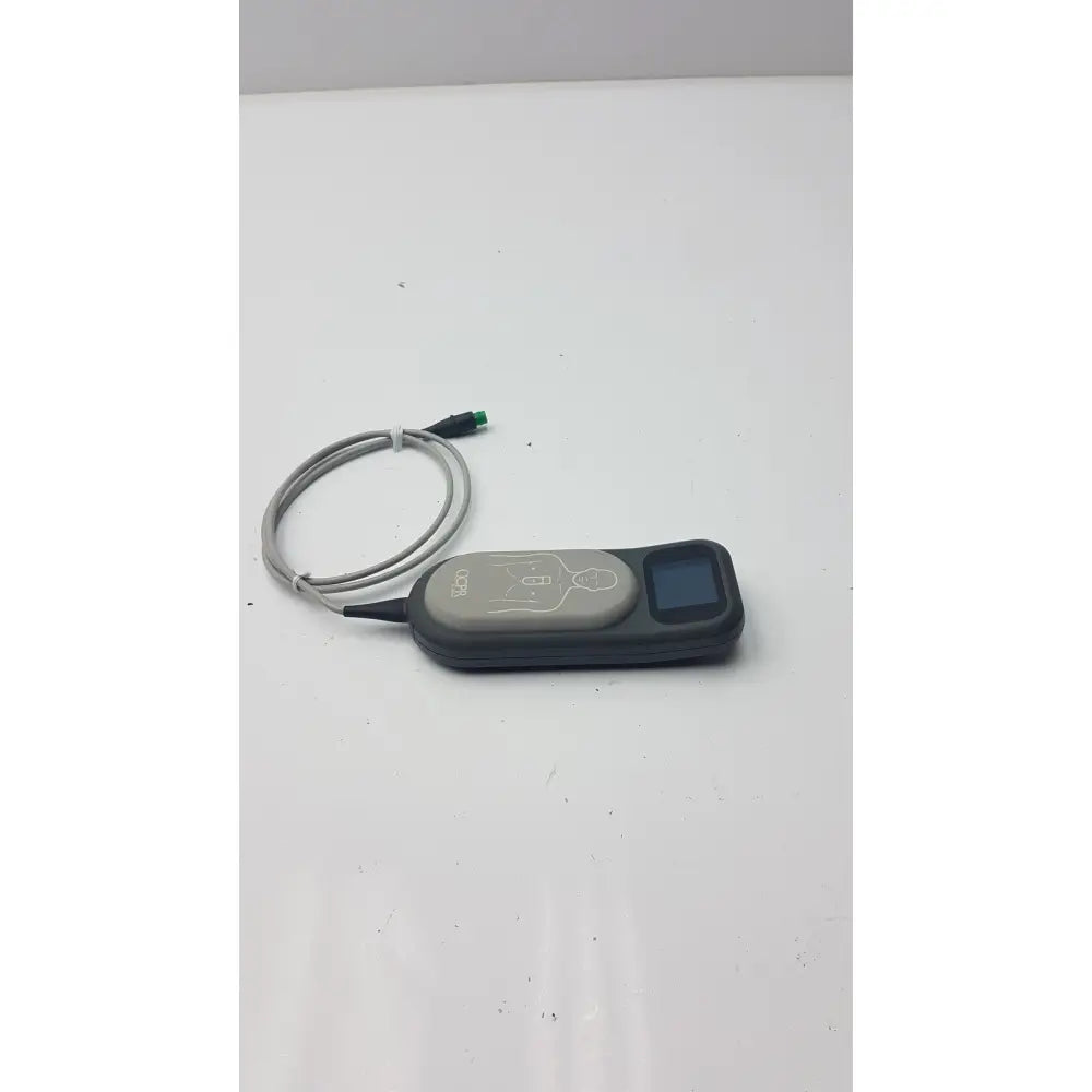 Gray and black laerdal cpr meter 453564257691 with small screen, coiled cable, and illustrated diagram on surface