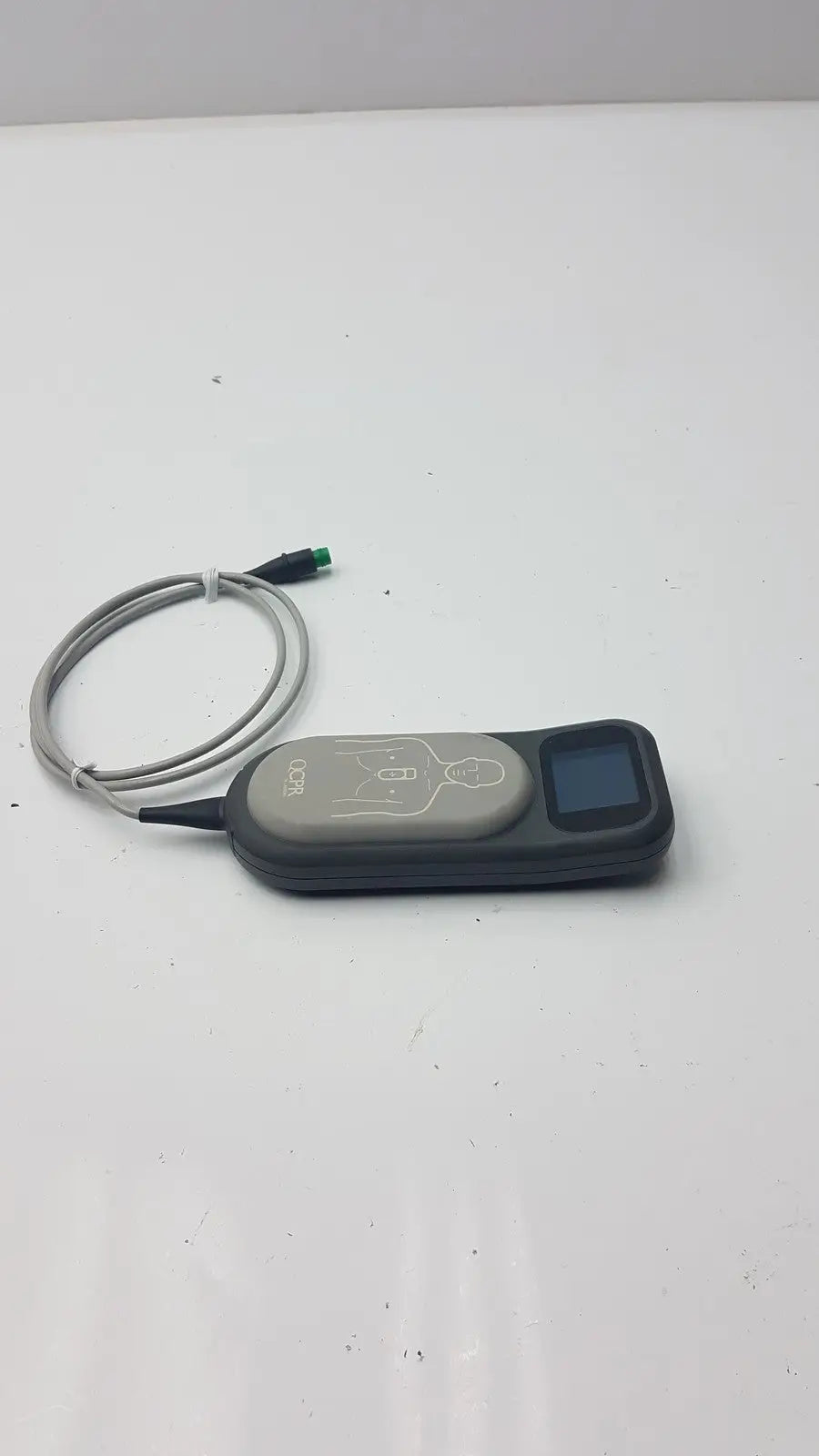 Gray and black laerdal cpr meter 453564257691 with small screen, coiled cable, and illustrated diagram on surface