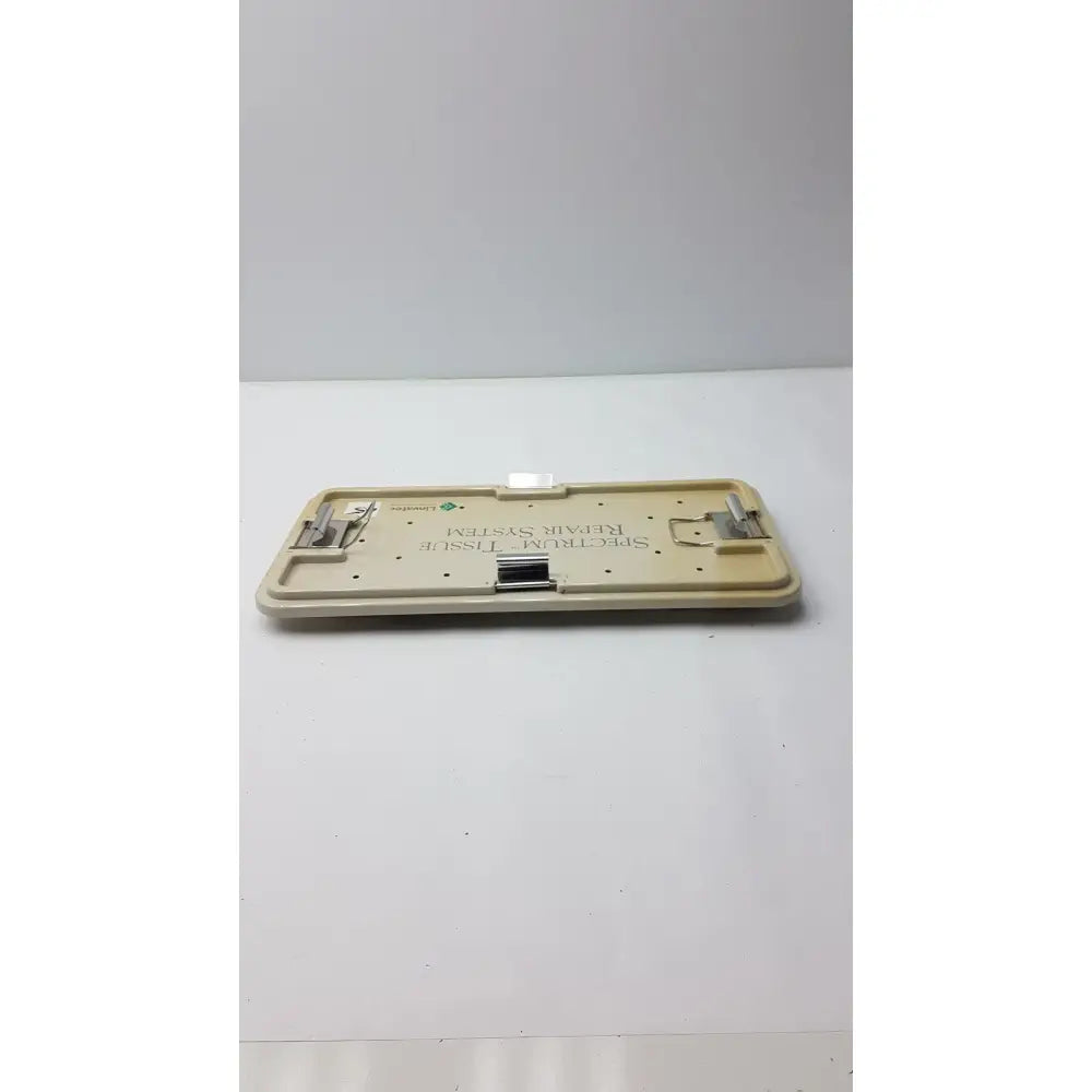 Beige plastic linvatec concept arthroscopy spectrum tissue repair system tray with metallic clamps and central slot