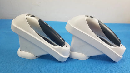 Two white and black handheld barcode scanners with silver accents resting in matching charging stands for reuse medical equipment