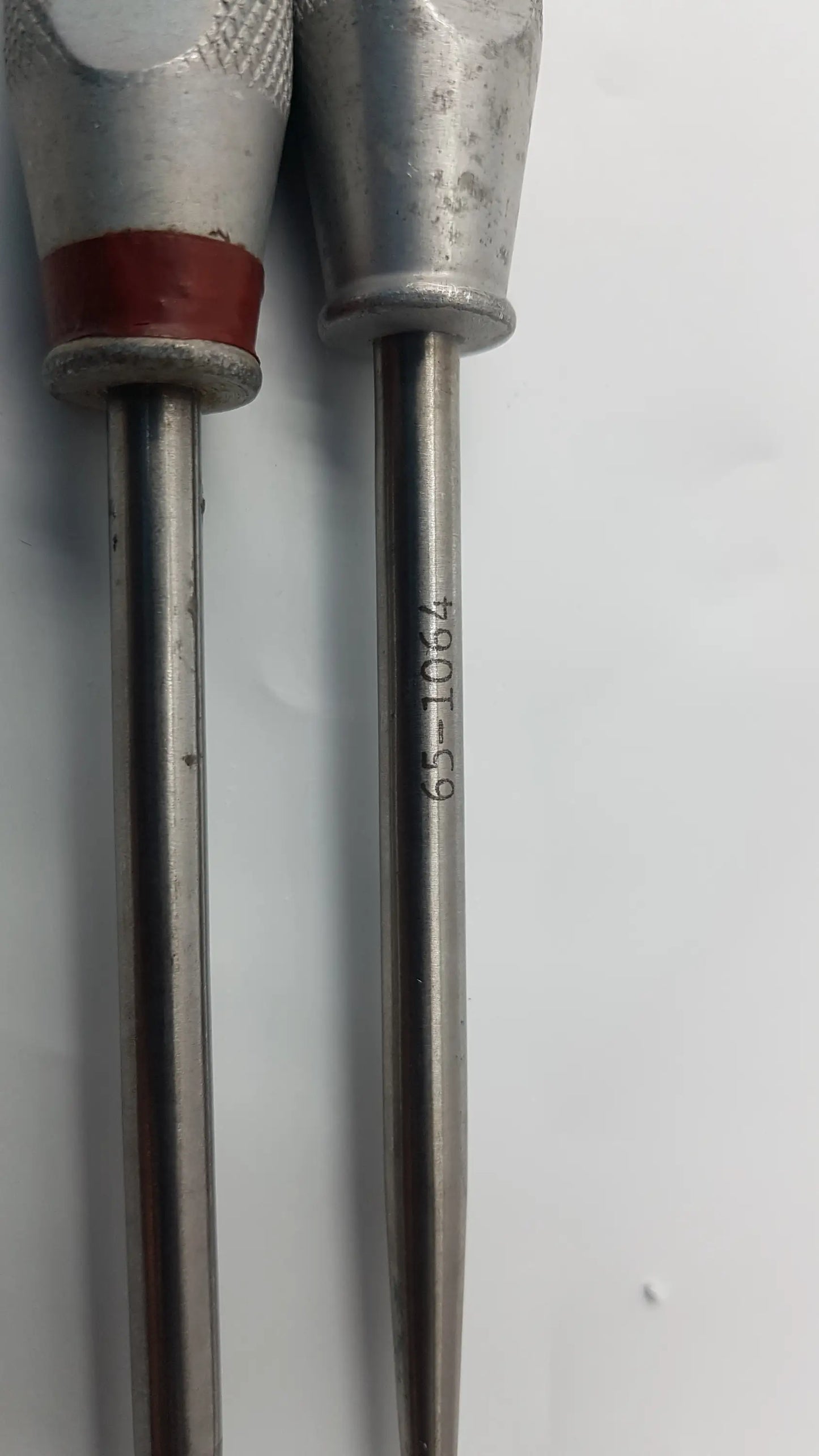 Two metallic codman 8710n osteophyte elevators with textured silver handles and red rubber grip for orthopedic surgical use