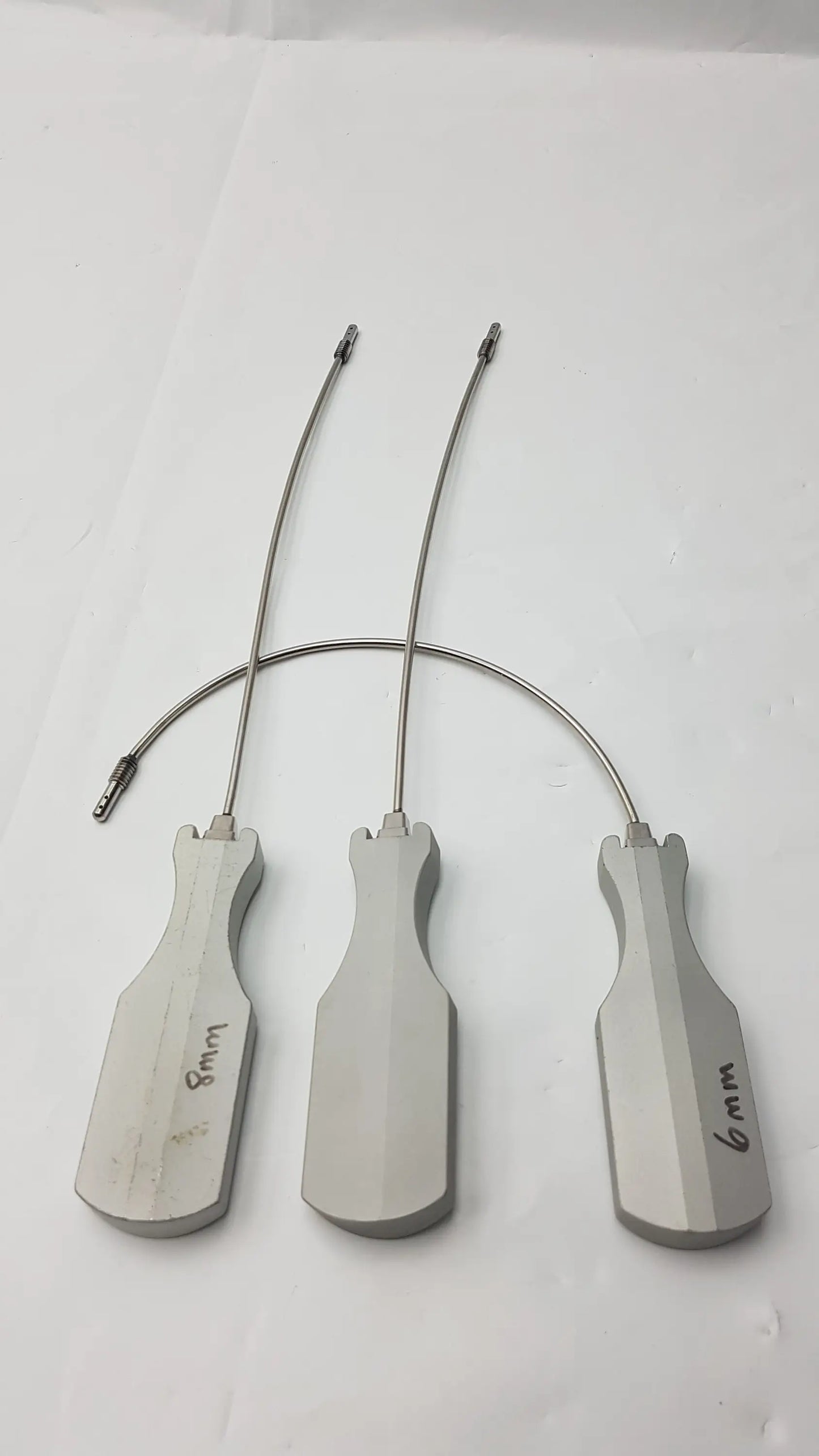 Three metallic surgical forceps with slender curved arms showing slight curve long and full curve long designs