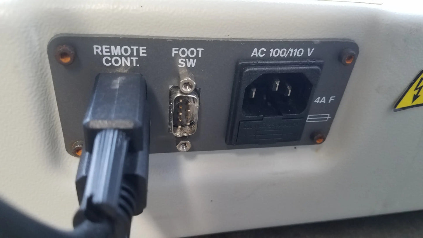 Black power cord plugged into 100/110v ac outlet on back panel of magstim tms therapy chair with articulating arm and stimulation coil