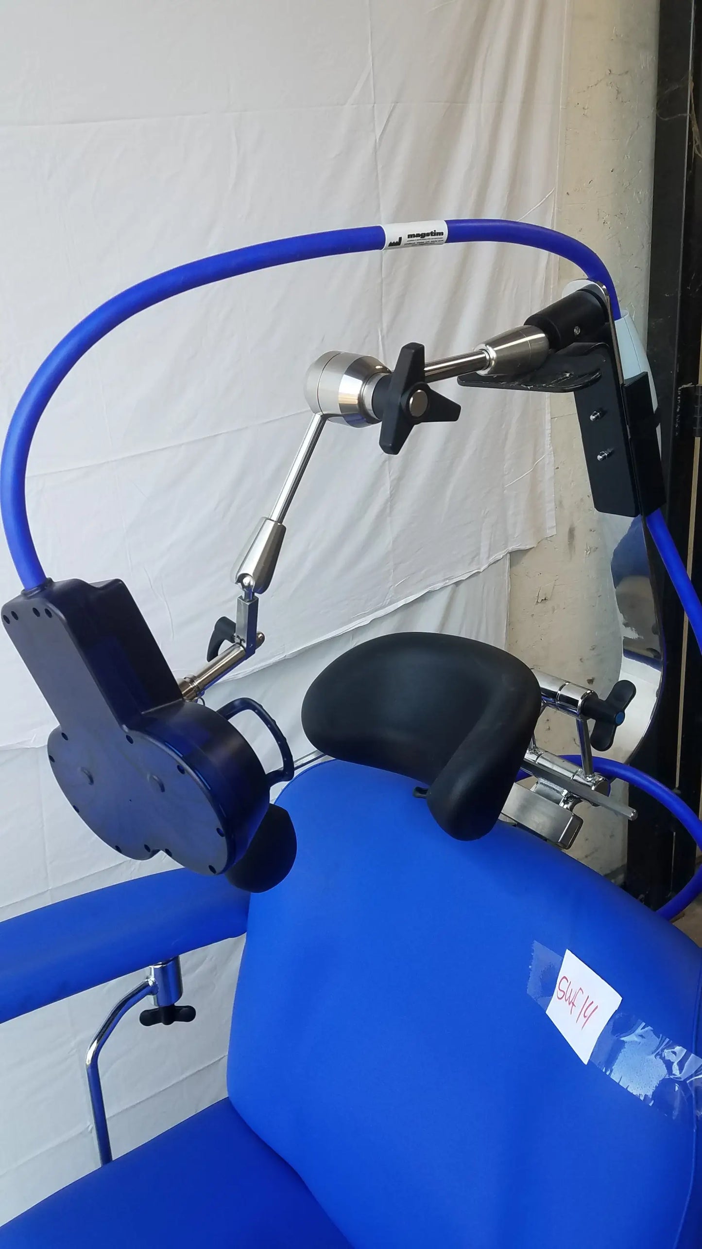 Blue magstim therapy chair with black cushioned pads, articulating arm, stimulation coil, and curved tube frame