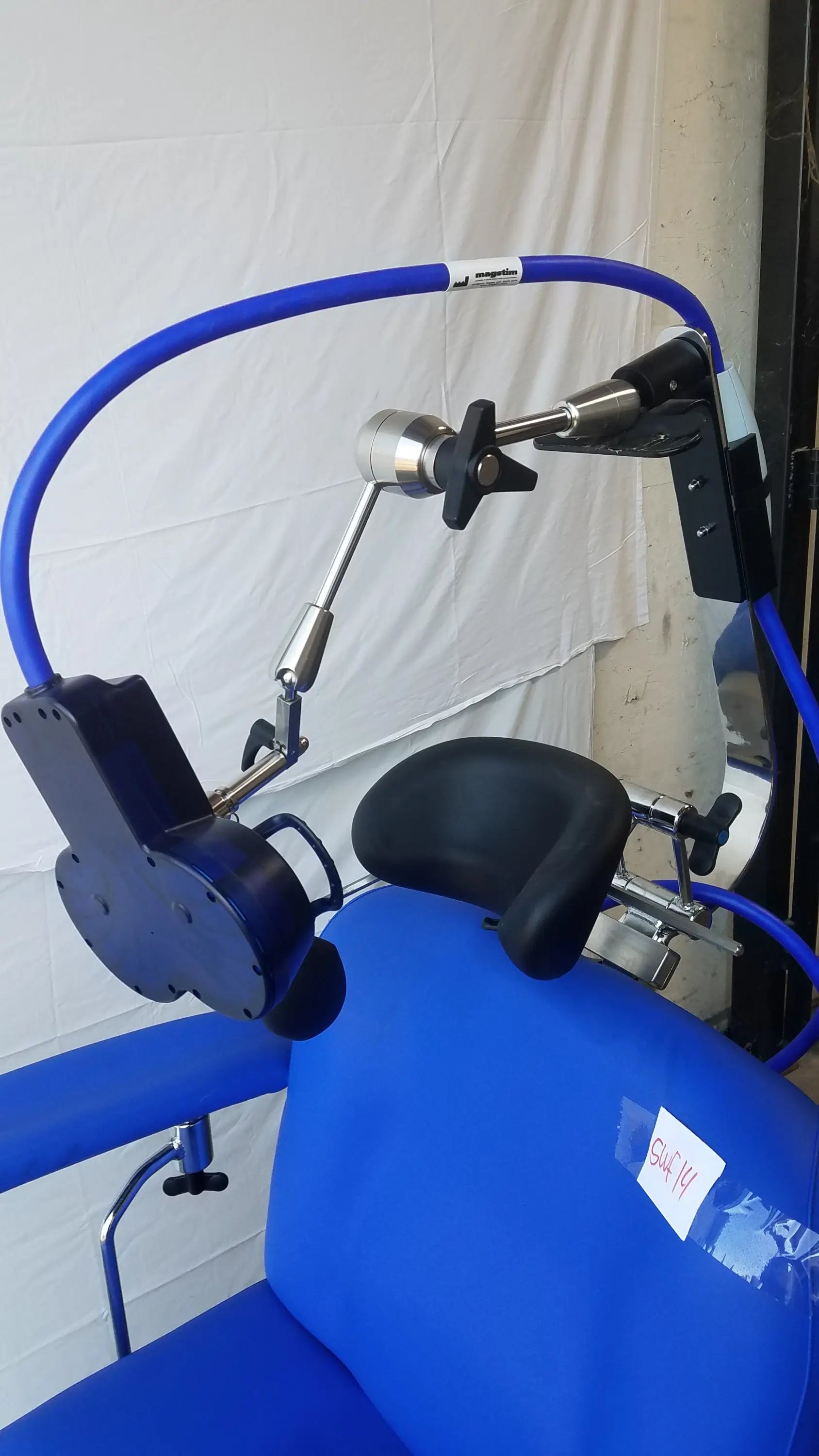 Blue magstim therapy chair with black cushioned pads, articulating arm, stimulation coil, and curved tube frame