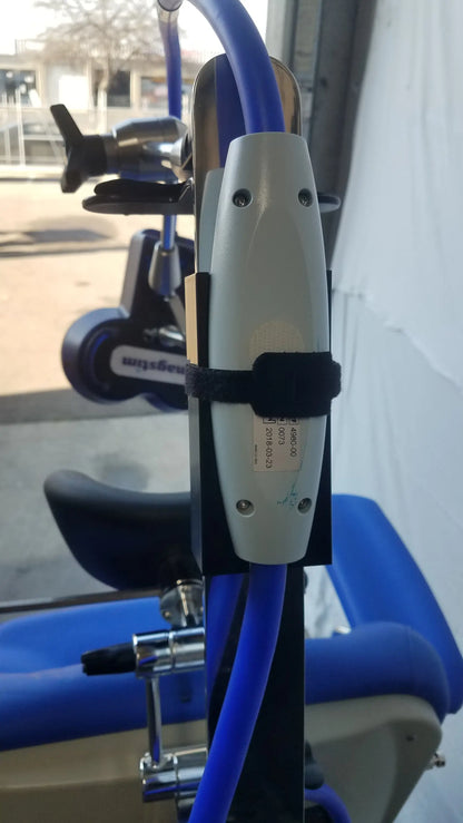 White cylindrical stimulation coil with black strap mounted on blue tubing attached to magstim therapy chair articulating arm