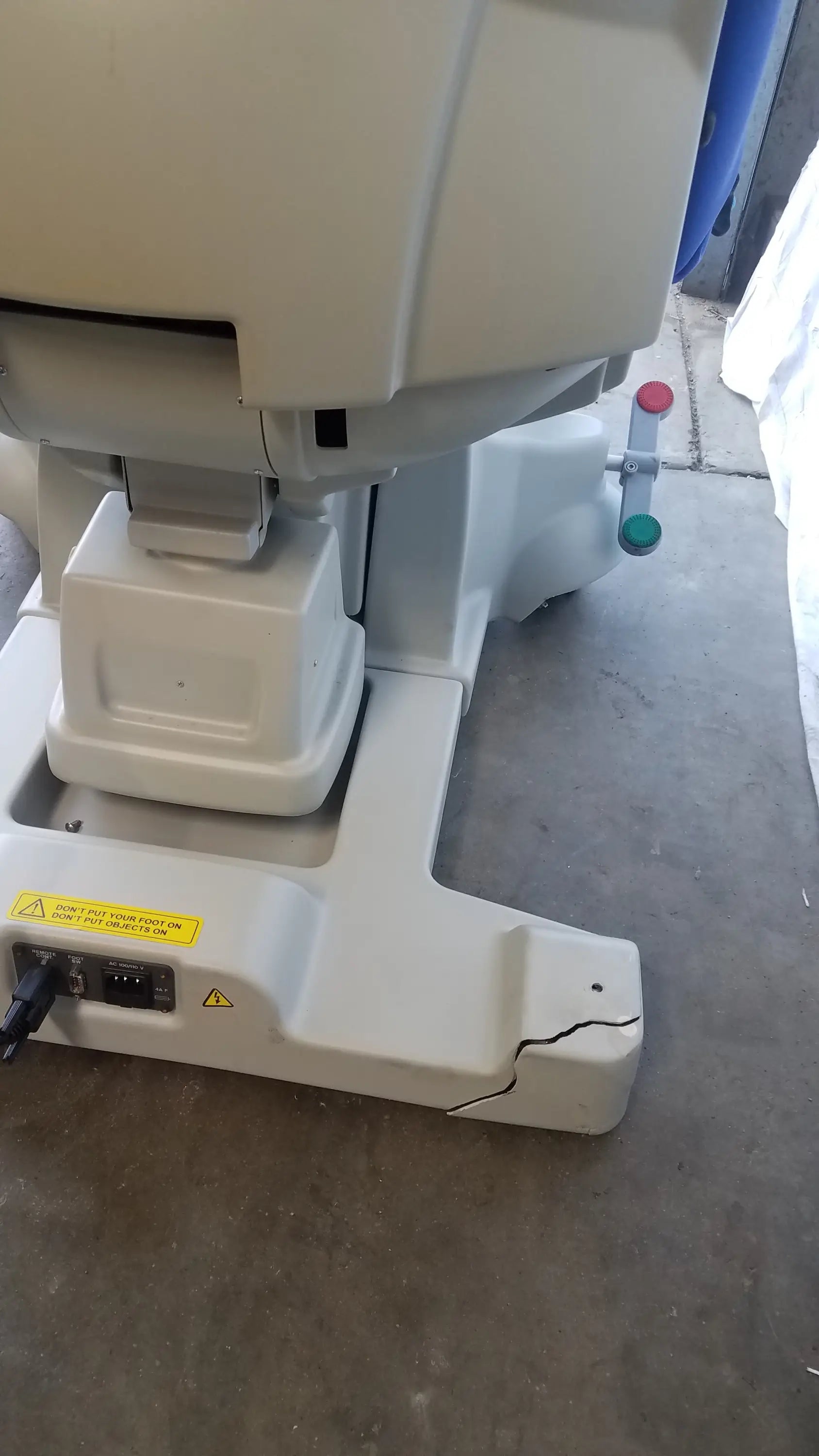 White plastic base of magstim tms therapy chair with cracked surface and electrical ports at the back side featuring articulating arm and stimulation coil