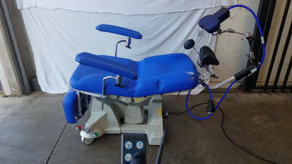 Blue Magstim TMS therapy chair with articulating arm, stimulation coil, adjustable armrests, padded seat, and gray wheeled base