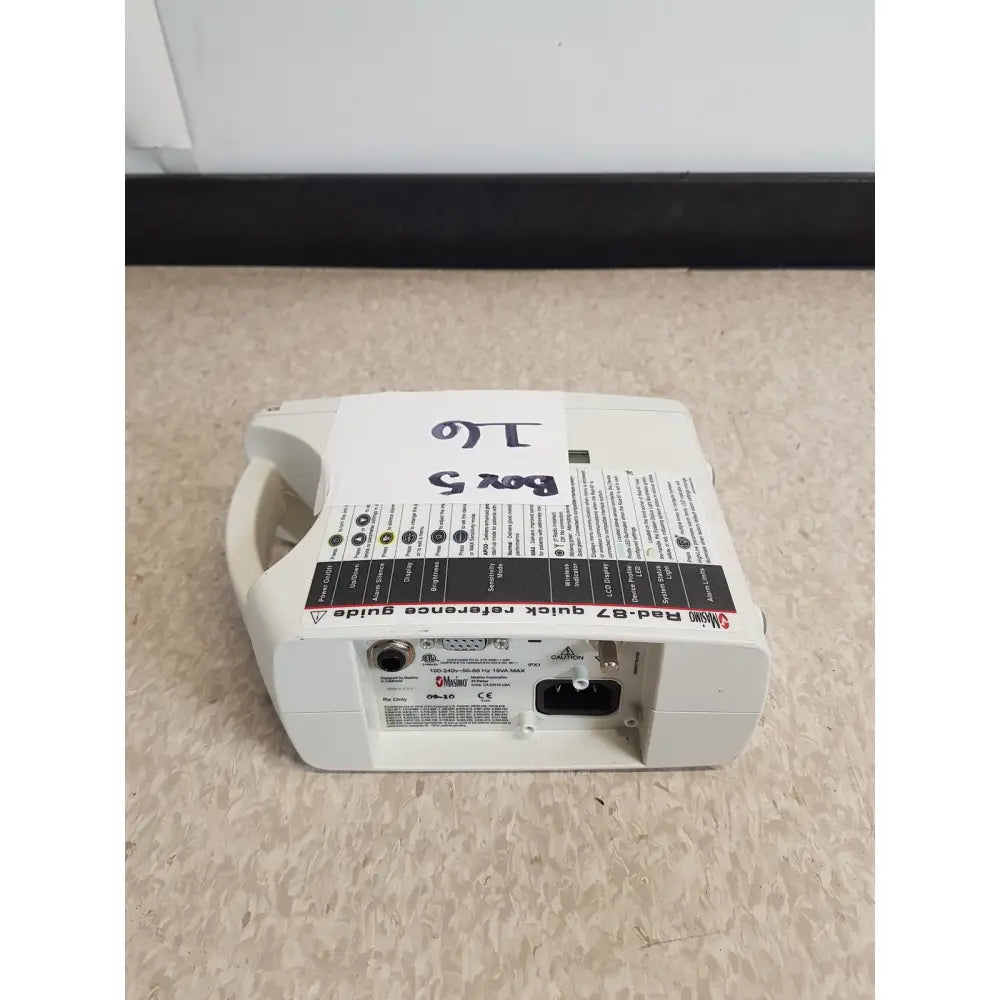 White plastic masimo set rainbow rad 87 pulse oximeter back side with black and red labeling power port and connectors