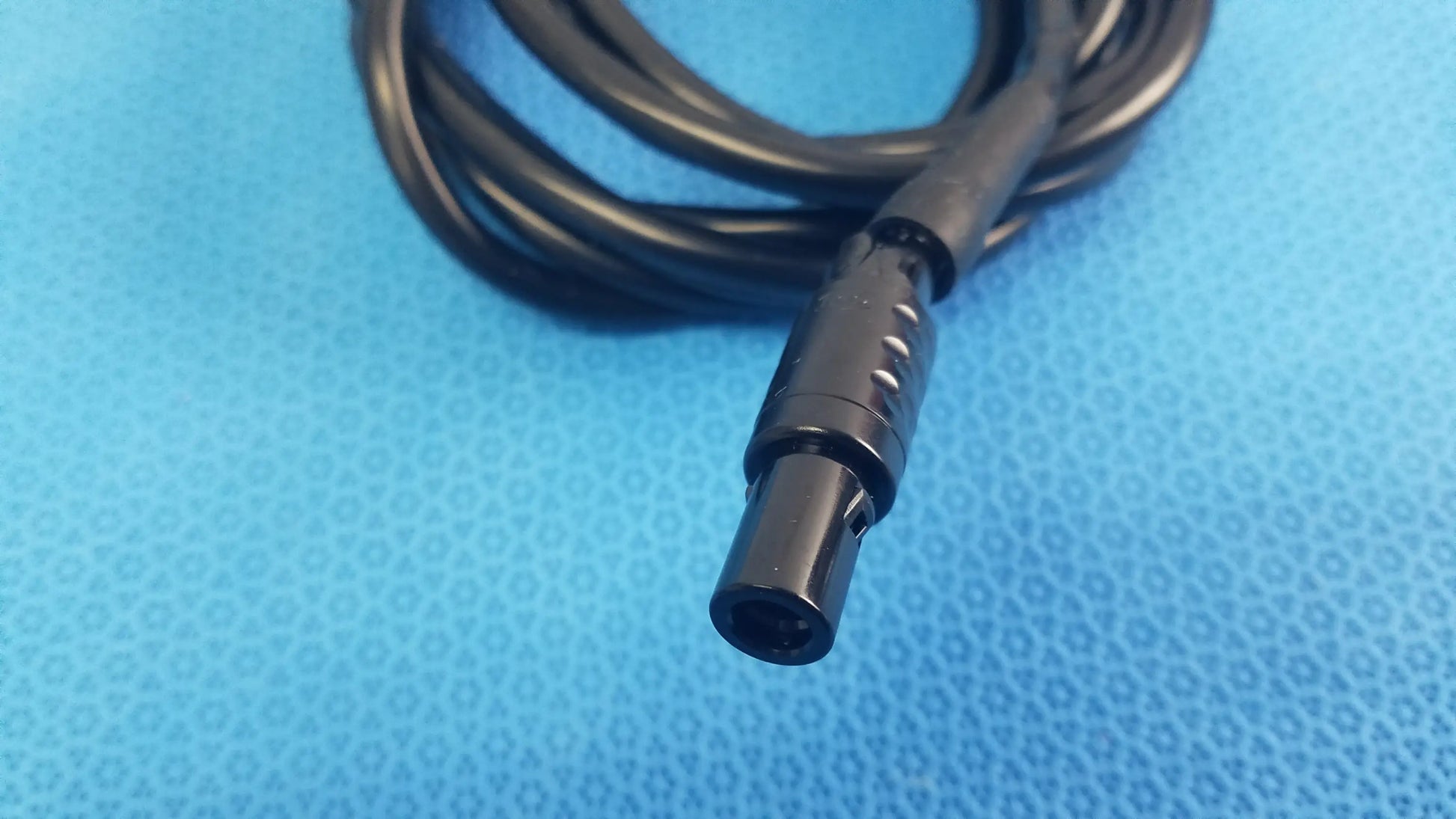Black coiled console extension cable with matte ridged connector featuring circular indentations for surgical handpiece use in medical equipment
