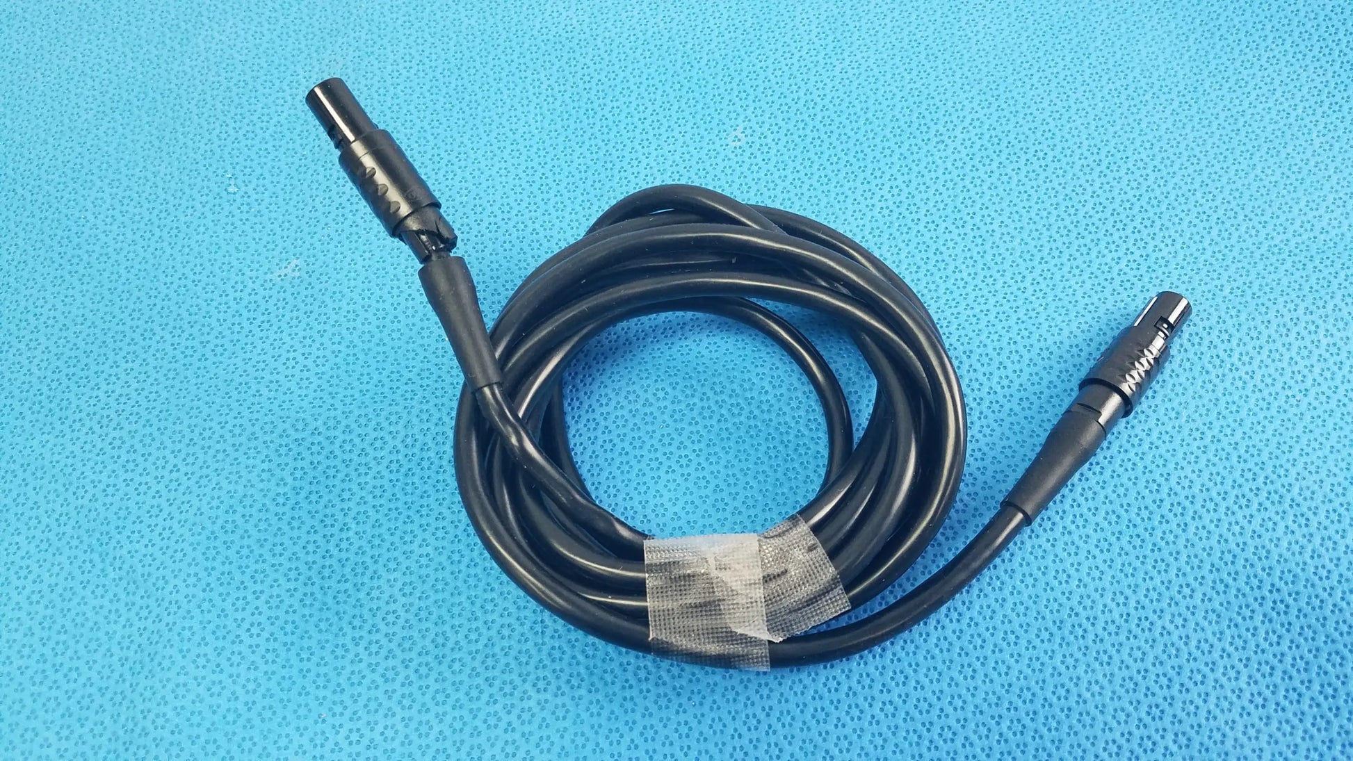 Black coiled medical surgical handpiece console extension cable with two metallic connectors for medical equipment use