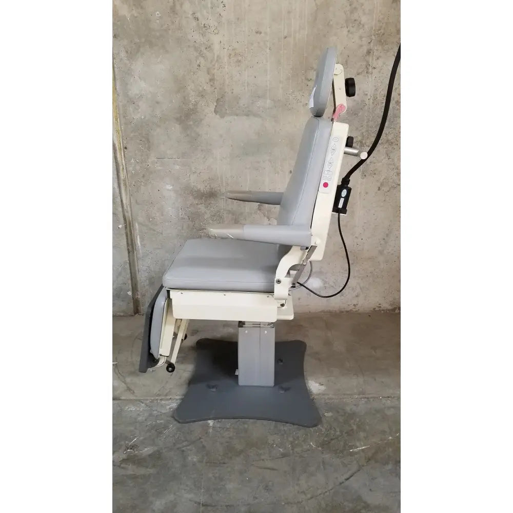 Gray upholstered medical technology industries power lift exam chair with adjustable headrest, armrests, and white metal frame