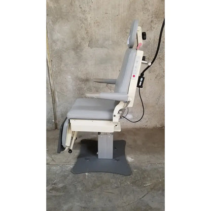 Gray upholstered medical technology industries power lift exam chair with adjustable headrest, armrests, and white metal frame
