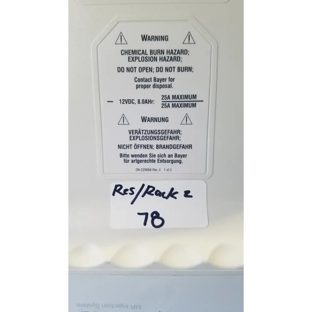 White plastic warning label with bilingual safety instructions and handwritten note on medrad spectris solaris mr injection system battery