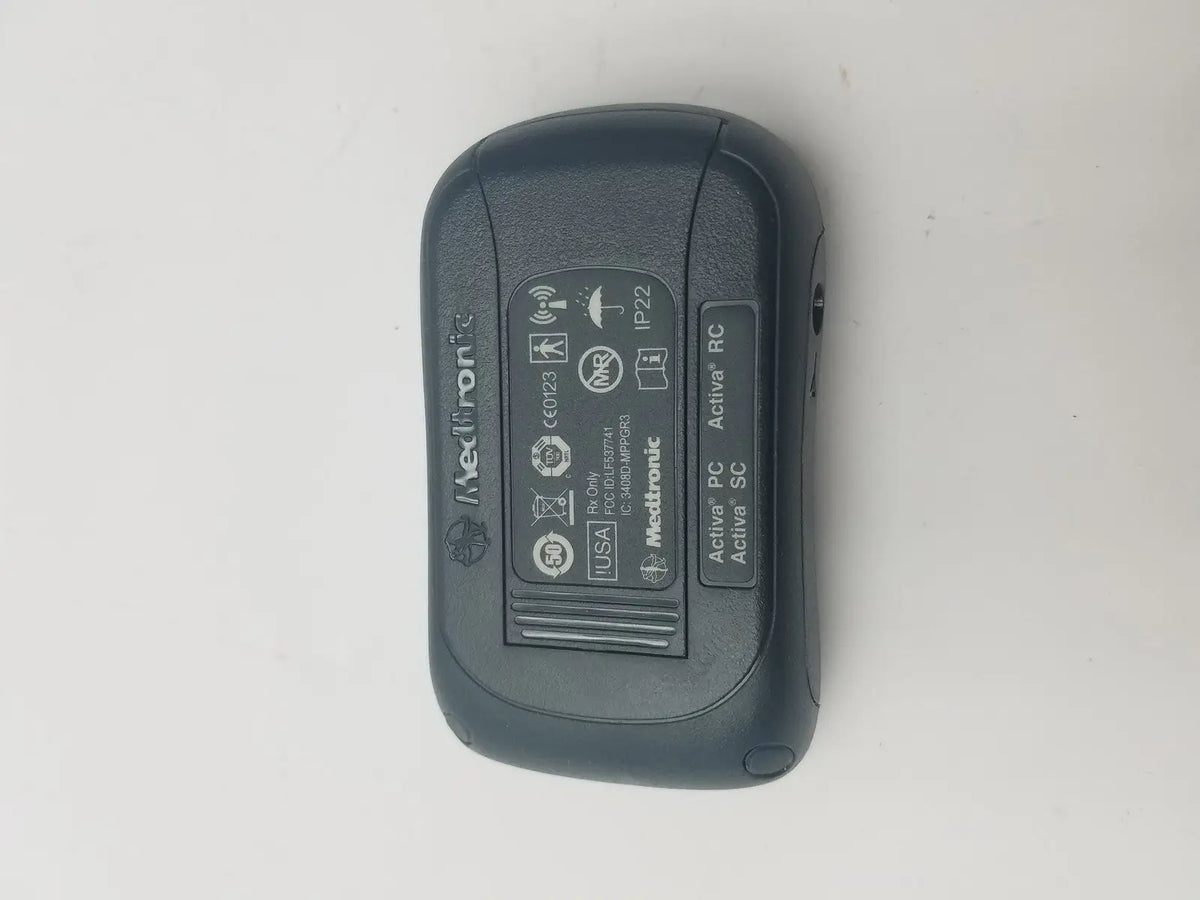 Black Medtronic Activa RC insulin pump with textured plastic casing and regulatory labels shown on back side in DBS patient programmer