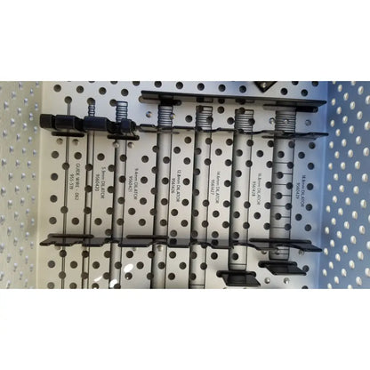 Black metal clamps with spring-loaded mechanisms on a perforated board in Medtronic 9568529 METRx II system dilators tray for reuse medical sterilization trays