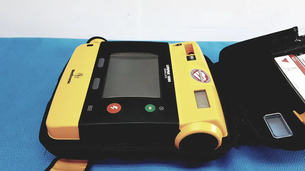 Yellow and black medtronic lifepak 1000 defibrillator with touchscreen display red green buttons and orange electrode pad holder for reuse medical use without battery or quik-pak pads
