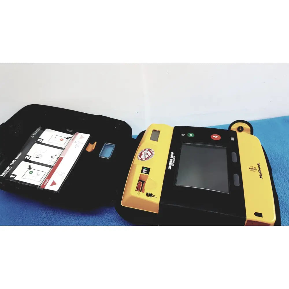 Yellow and black medtronic lifepak 1000 defibrillator with touchscreen display red green buttons and orange electrode pad holder for reuse medical use without battery or quik-pak pads