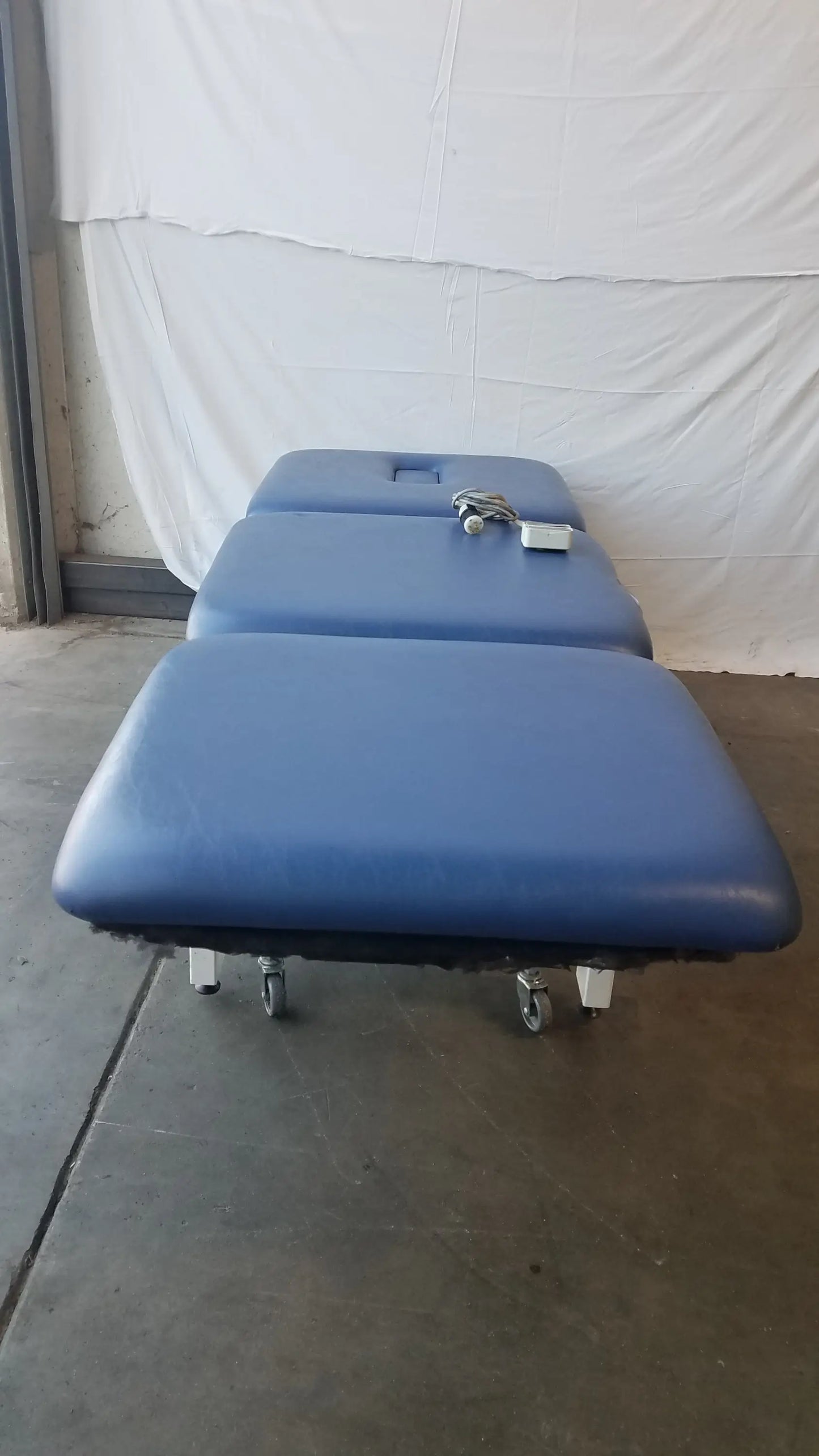 Blue padded metron 3-section electric treatment table with segmented sections and caster wheels for electric treatment