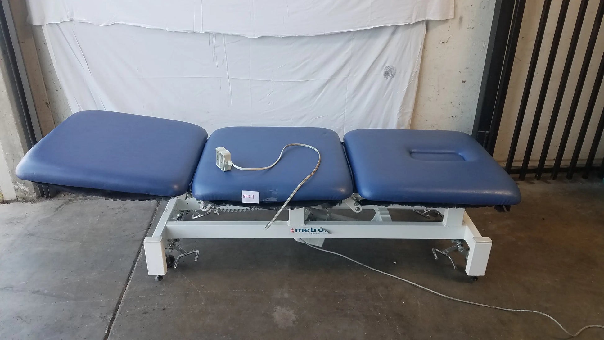 Blue padded three-section metro electric treatment table with white metal frame and wheels for medical use