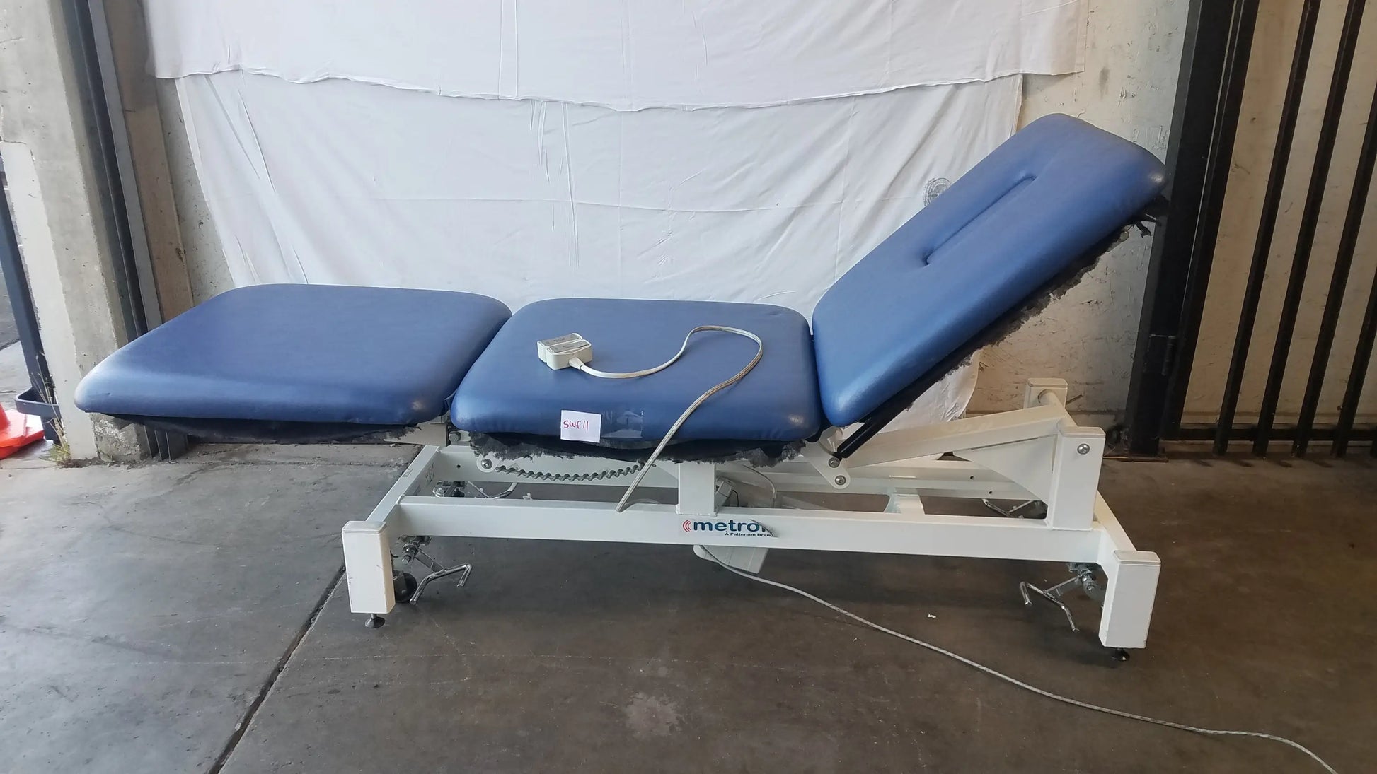 Blue padded three-section metro electric treatment table with white metal frame and casters for adjustable treatment