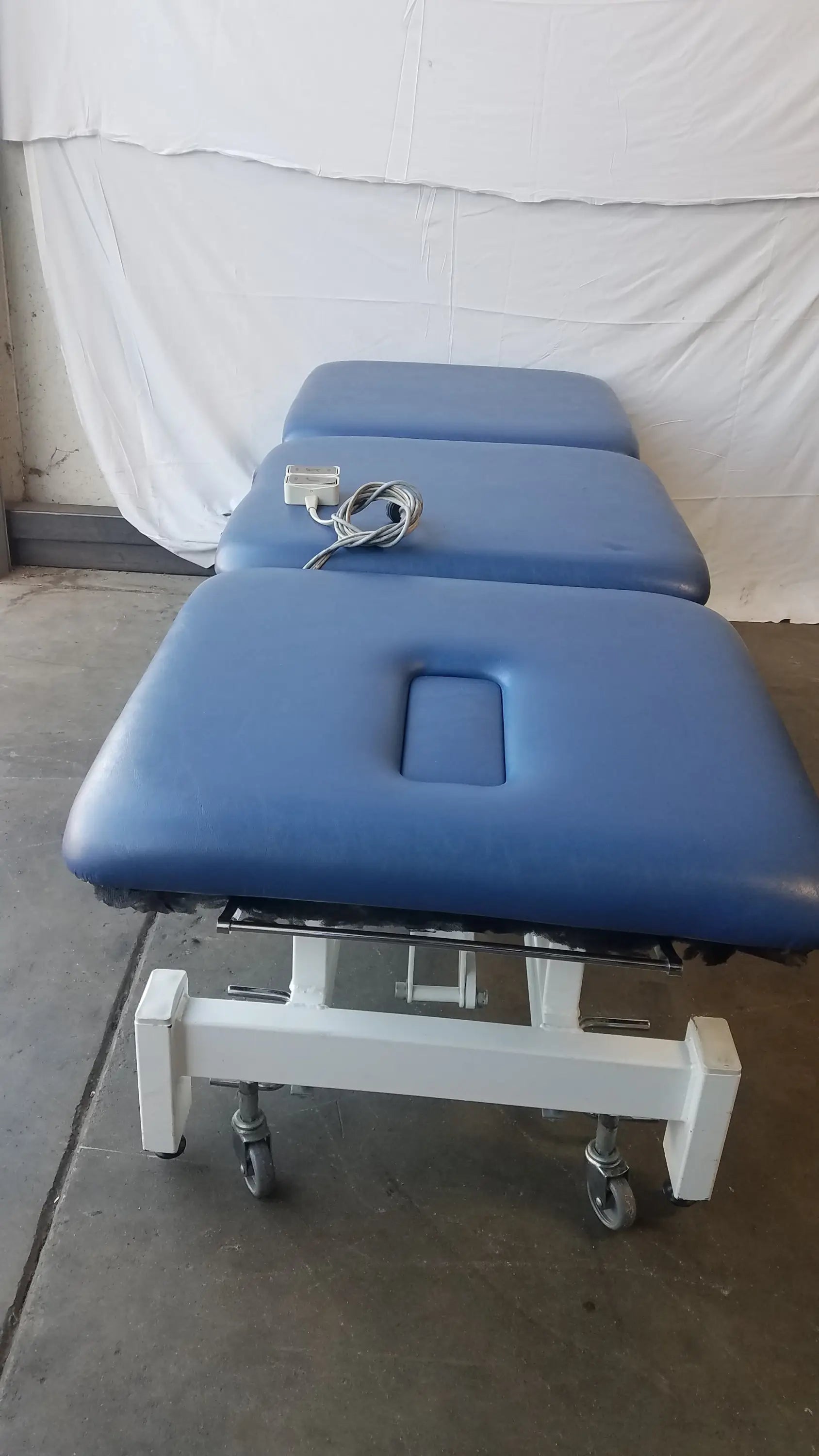 Metron 3-section electric treatment table with blue padded surface white metal frame and casters for easy mobility