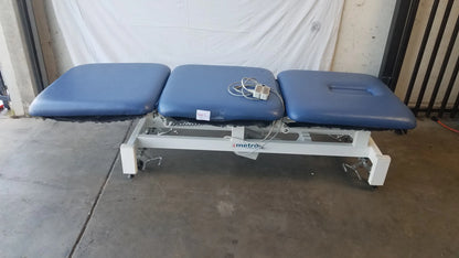 Blue three-section electric treatment table with white metal frame and casters branded metrox for medical use