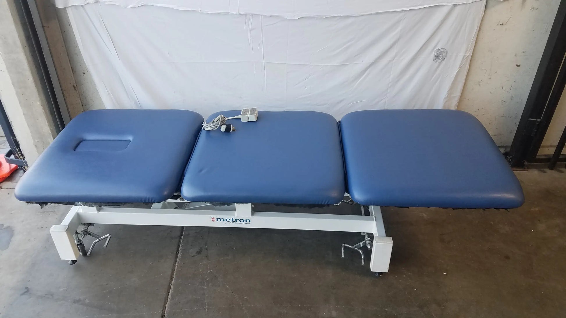 Blue three-section electric treatment table with white metal frame casters branded metron for medical use