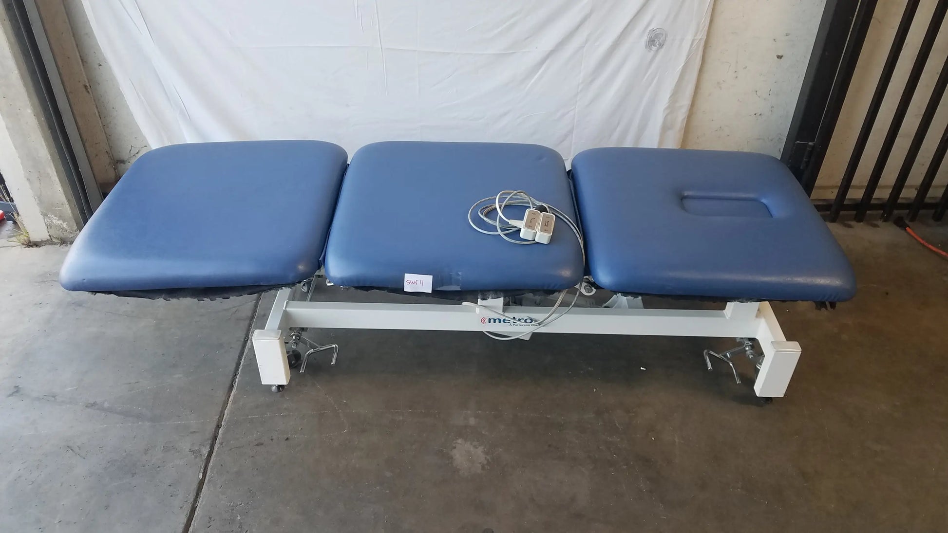 Blue three-section electric treatment table with white metal frame and casters for adjustable electric treatment use