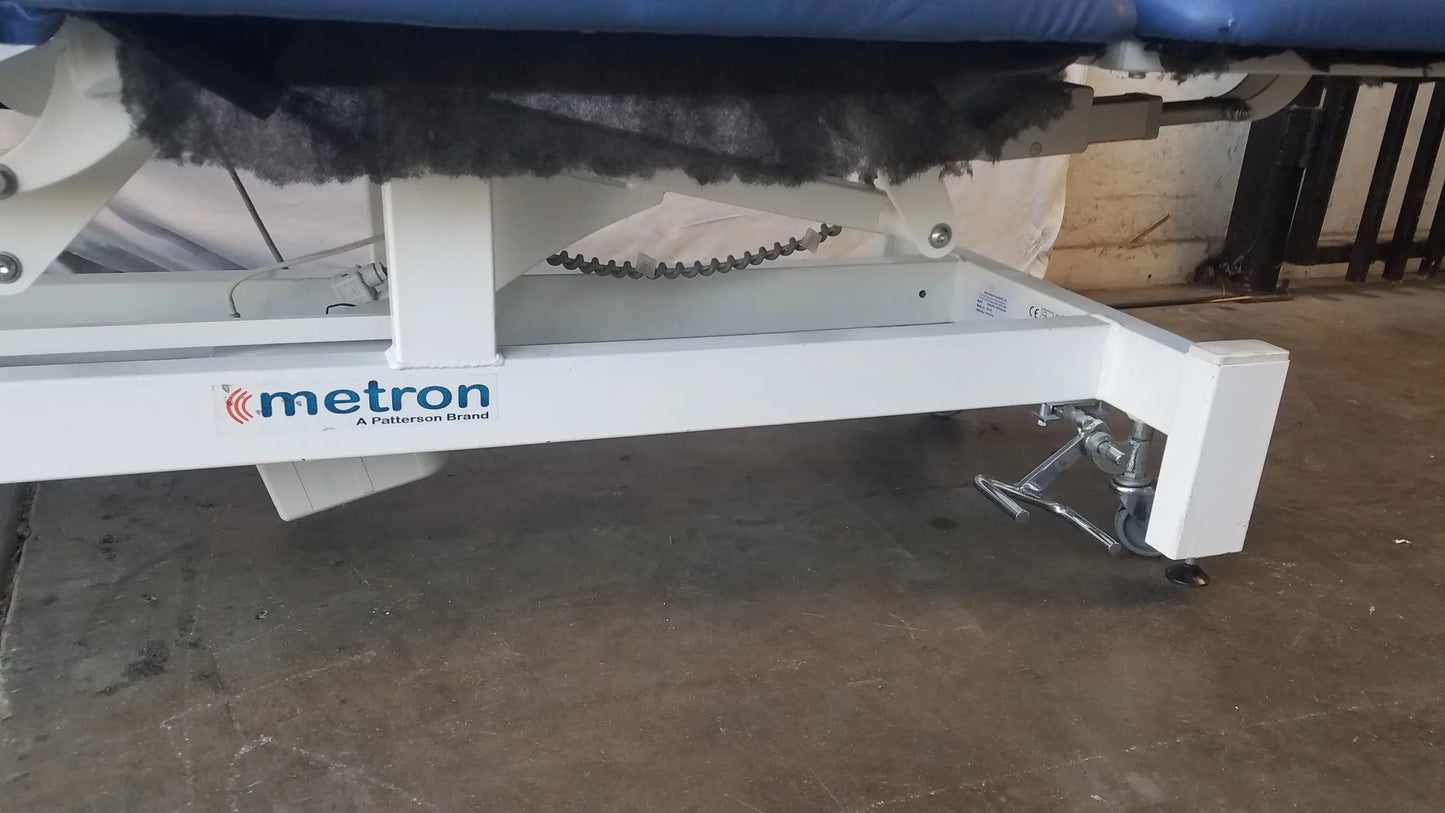 White metal frame metron 3-section electric treatment table with blue padded surface and black protective cover