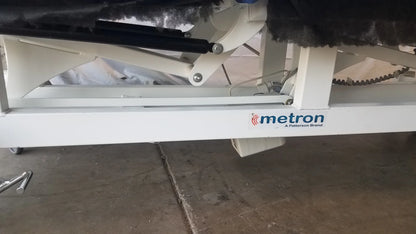 White metal frame of metron 3-section electric treatment table with black hydraulic lift and chain drive system visible from back side