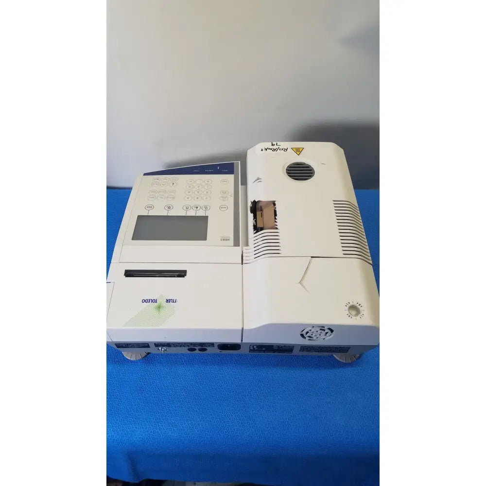White mettler toledo hr83-p halogen moisture analyzer with blue control panel and black ventilation slits showing merk branding