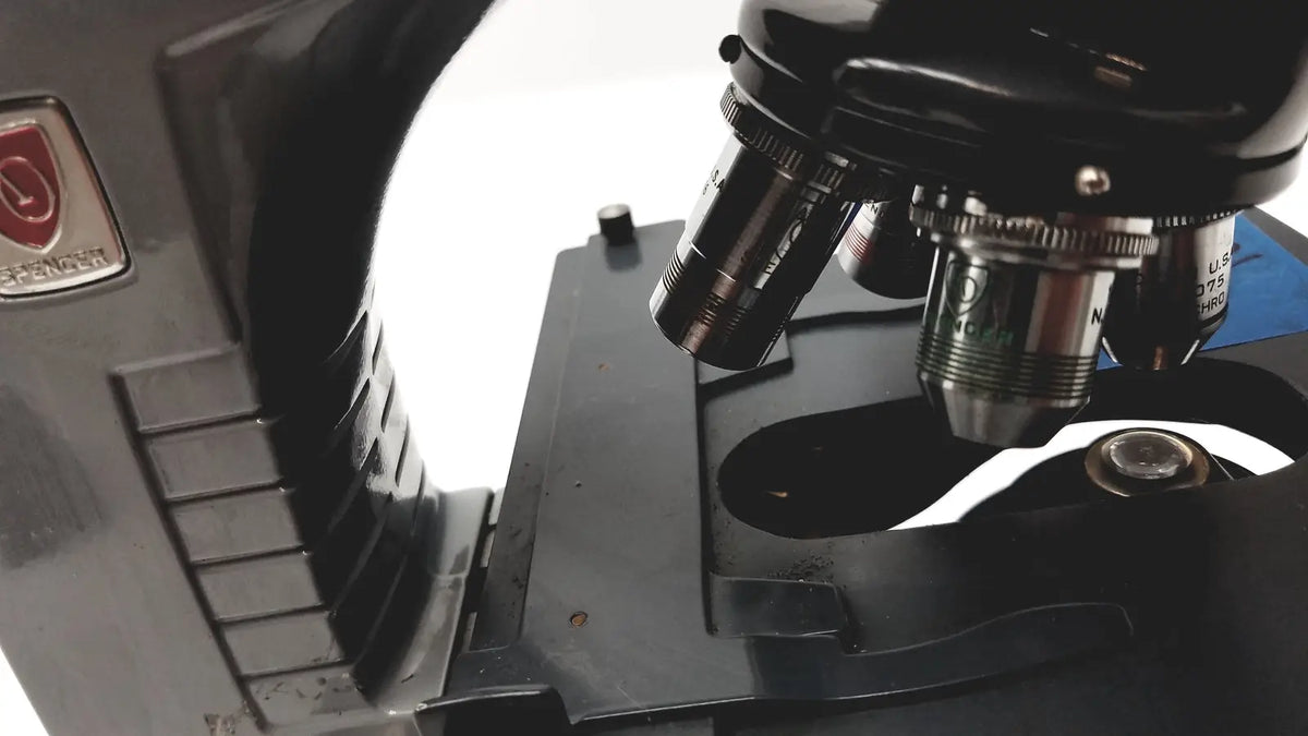Black metal microscope american optical spencer with silver-toned objective lenses and red logo plaque on the side