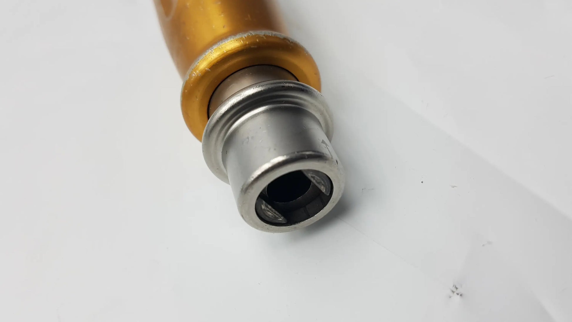 Gold-colored cylindrical handle with silver metallic threaded end cap of midas rex legend 1000 rpm ad03 perforator driver