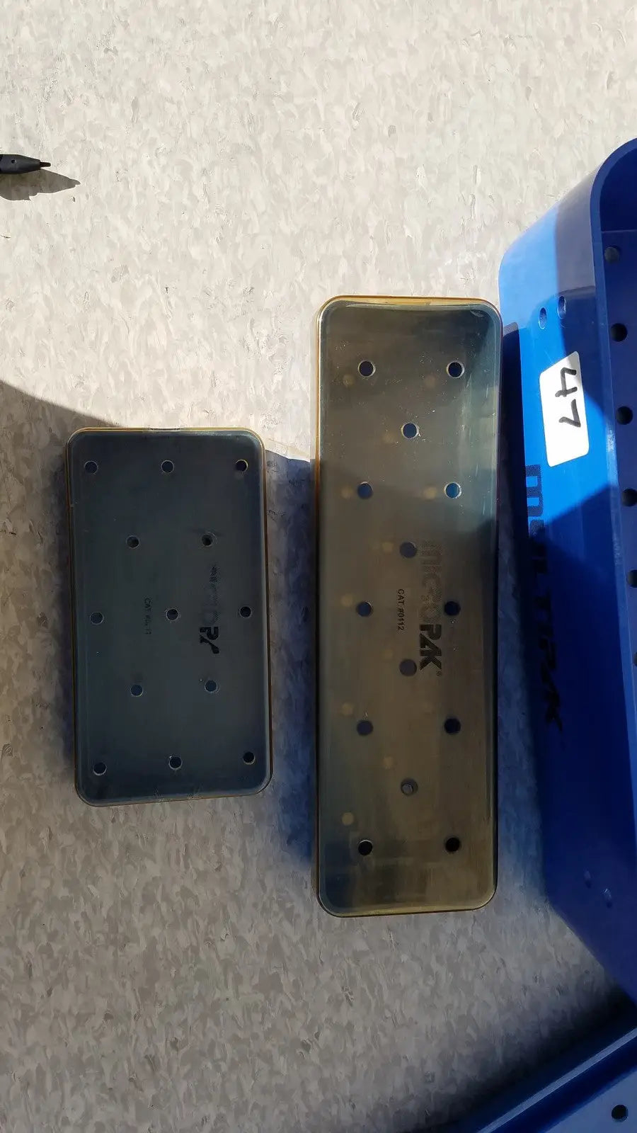Two translucent rectangular plastic sterilization trays with circular holes and embossed branding multipak 5006-02-000p