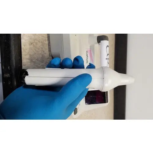 White plastic otoscope with black tip held in blue latex gloves for natus neurology freedop xld004 examination