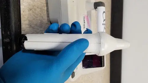 White plastic otoscope with black tip held in blue latex gloves for natus neurology freedop xld004 examination