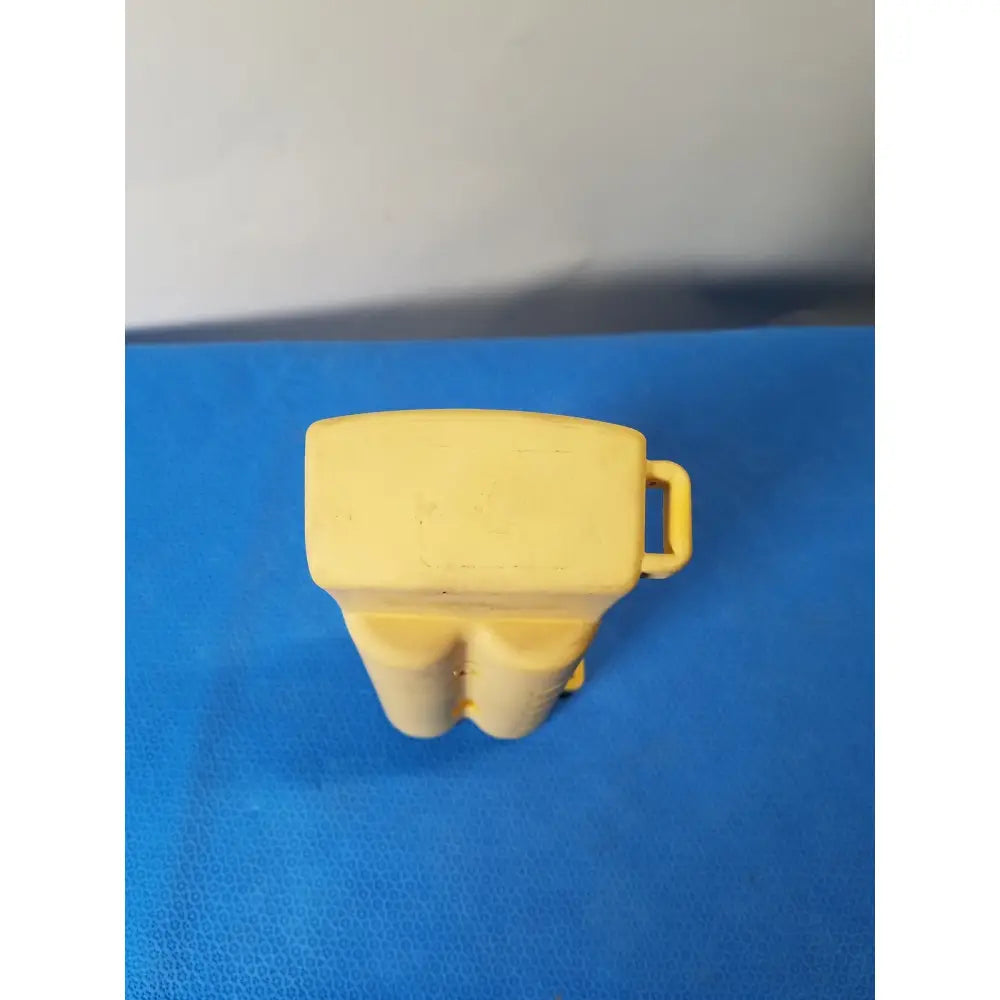 Yellow plastic toy figure with rectangular head and two rounded legs alongside nellcor puritan bennett portable pulse oximeter with case