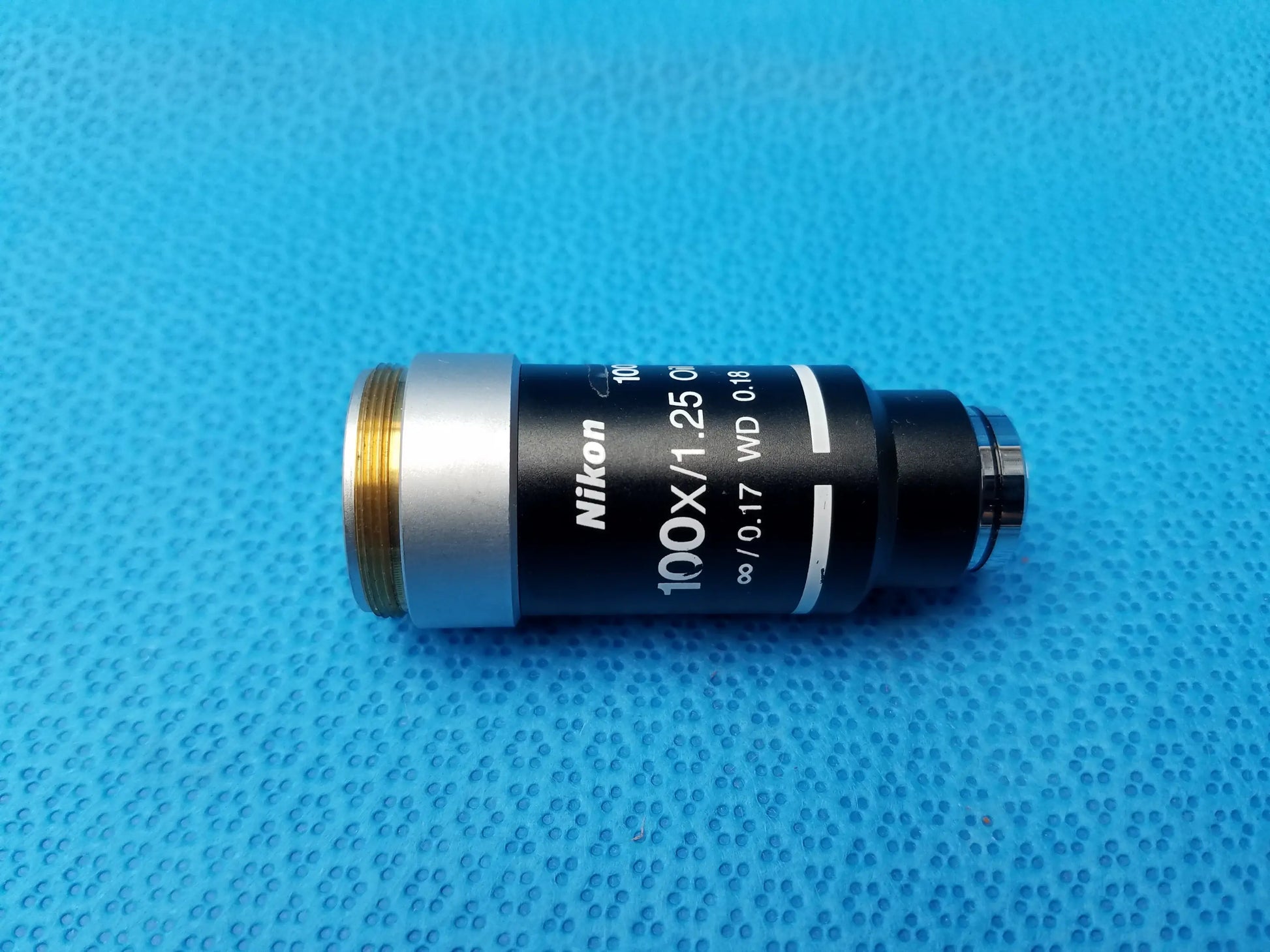 Nikon 100x 1.25 microscope objective with black body, silver ring, and gold threading for compatible Nikon microscopes