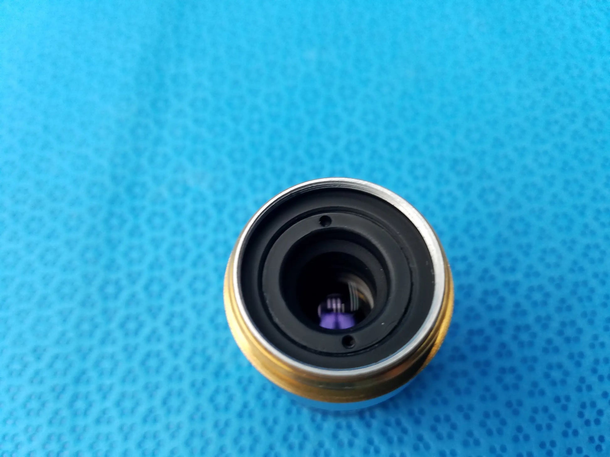 A circular metallic Nikon E Plan microscope objective with gold outer ring and black inner components showing numerical aperture