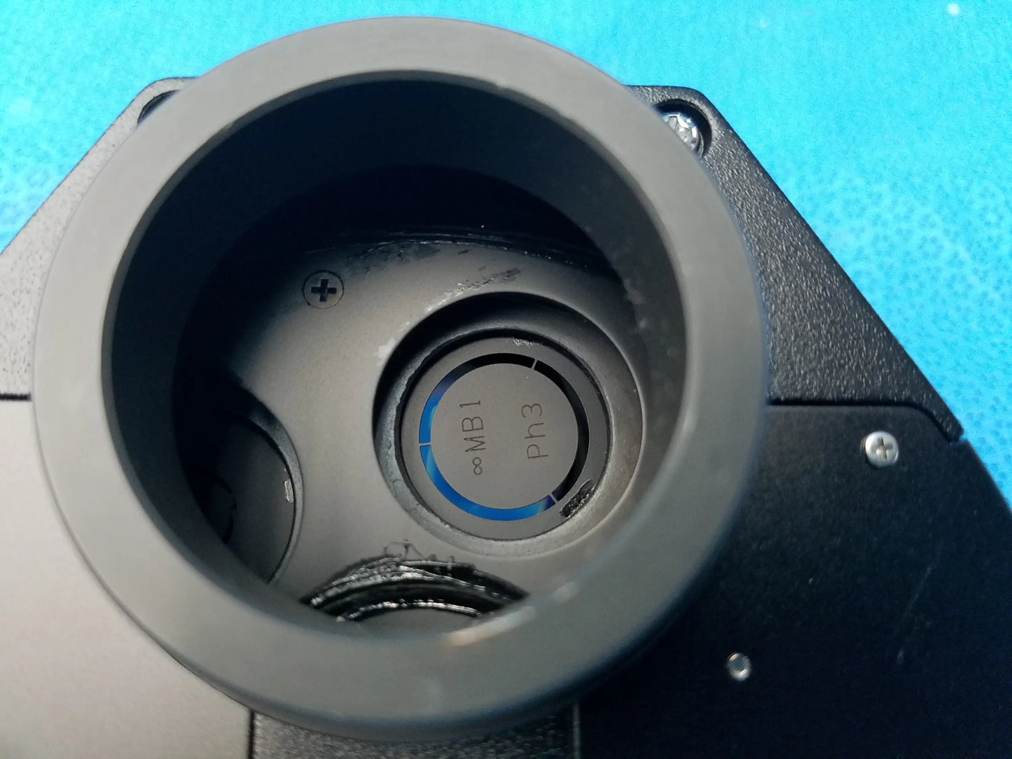 Gray circular dial with blue illuminated phase contrast markings set into black mechanical housing of nikon microscope turret