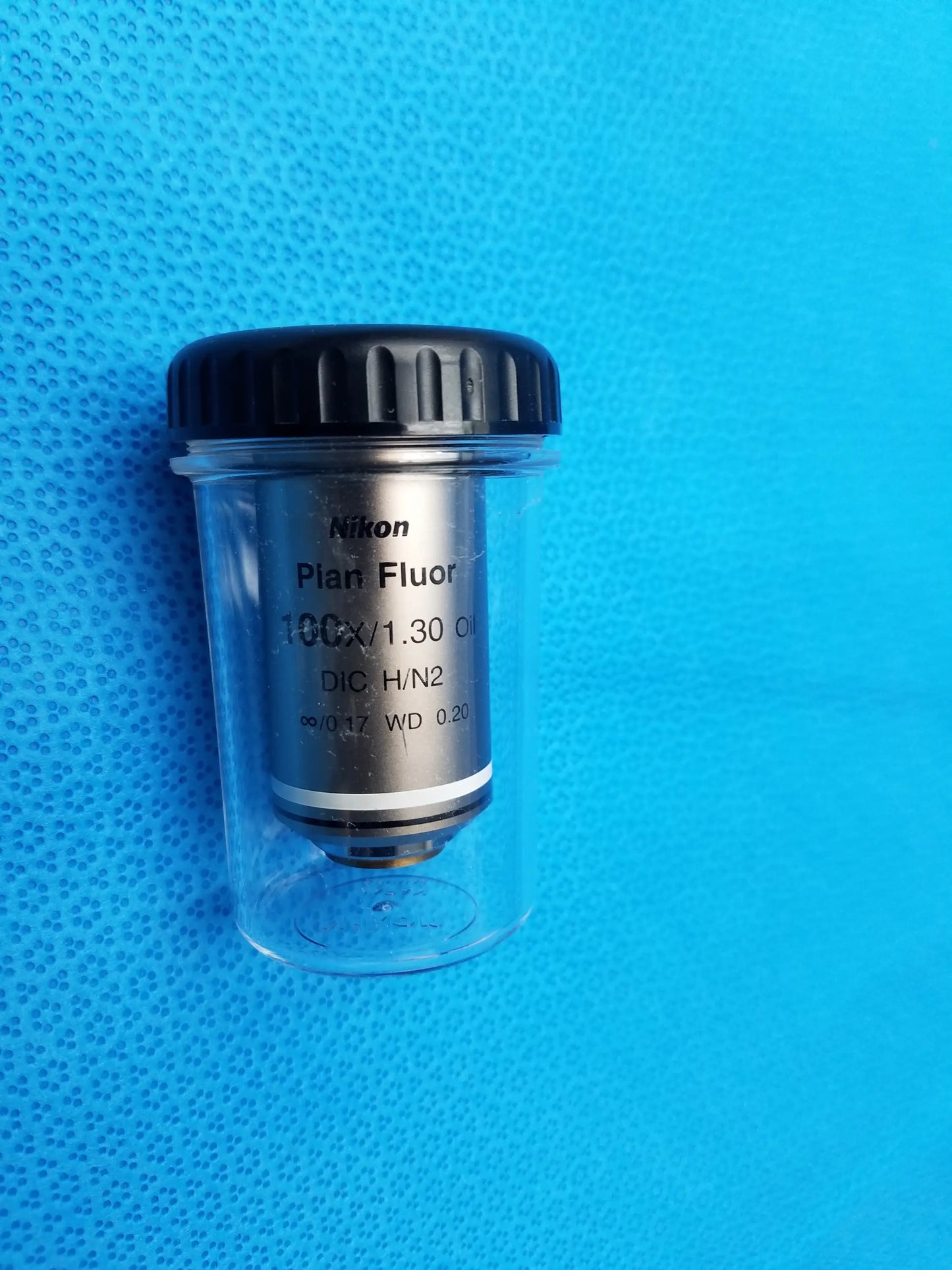 Nikon plan fluor 100x 1.30 oil immersion microscope objective with black ribbed cap and metallic body in clear container compatible Nikon