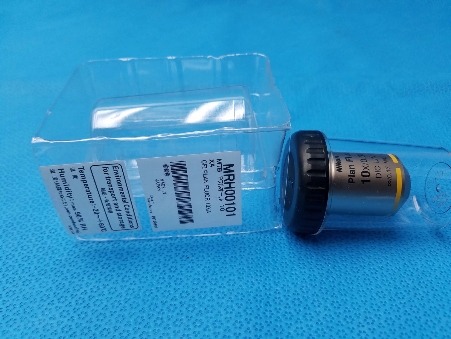 Nikon plan fluor 10x/0.30 microscope objective lens with yellow ring and 16 mm working distance on blue surface