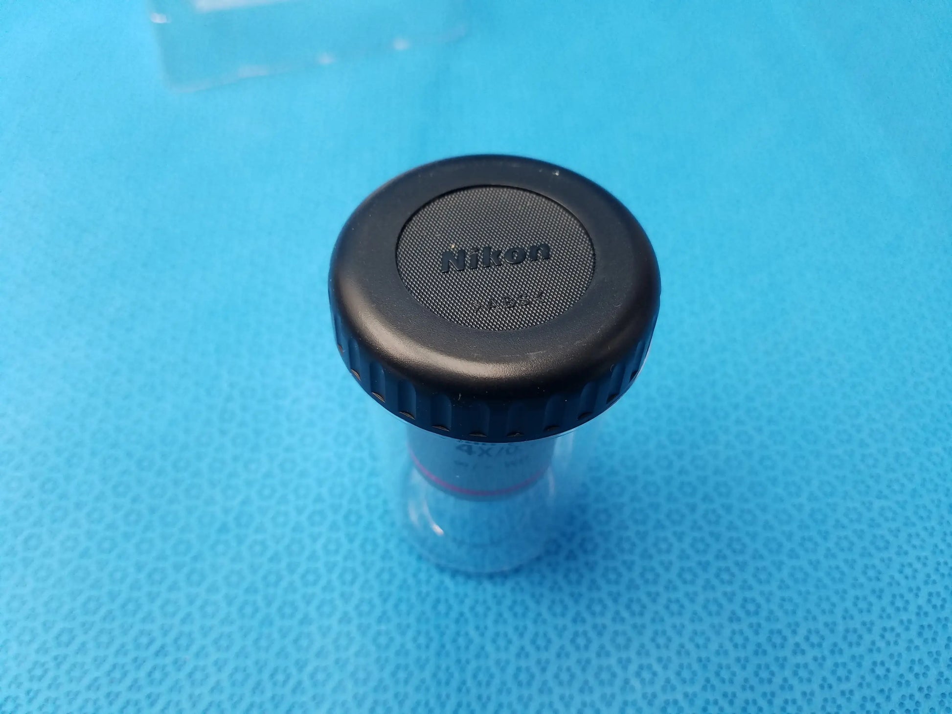 Black Nikon lens cap with textured grip and silver logo on clear base for compatible Nikon plan fluor microscope objective