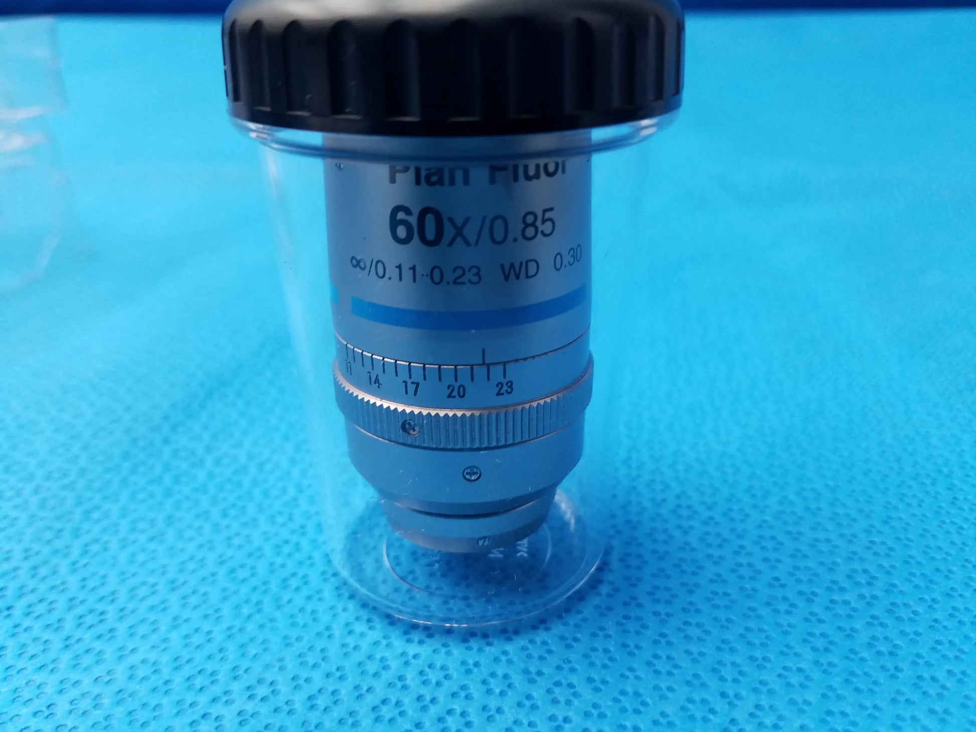 Silver-colored Nikon plan fluor 60x/0.85 microscope objective with black cap in clear protective casing compatible Nikon